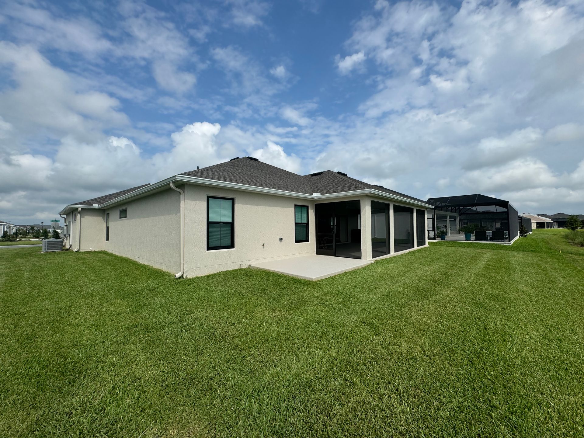 Single-story house with a light-colored exterior and a dark-tiled roof, set against a bright blue sky and green lawn.