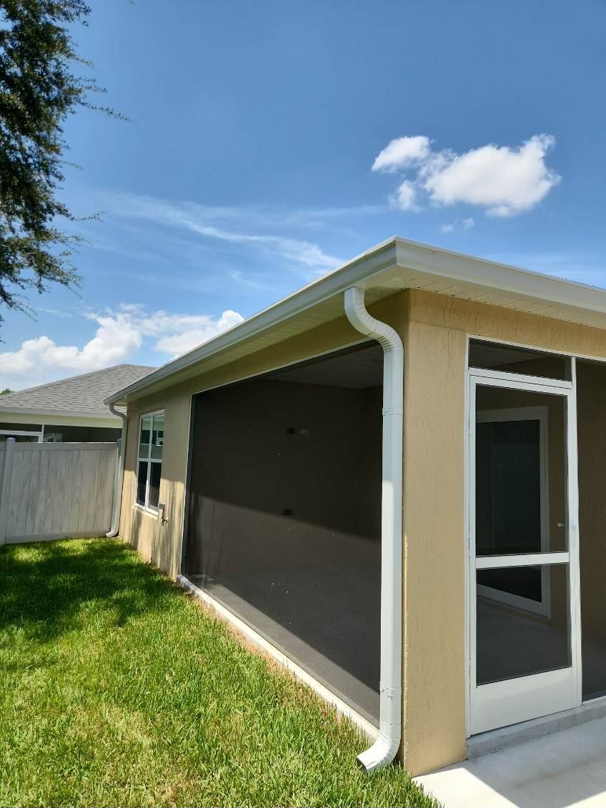 Tan stucco house with white gutters, screened patio, and green lawn under a blue sky.