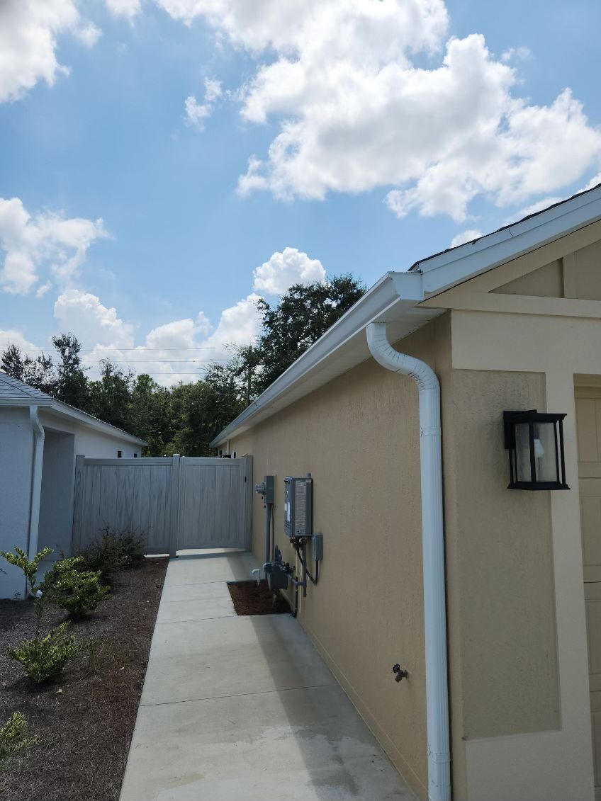 Beige house with white gutters, sidewalk, and blue sky with clouds.