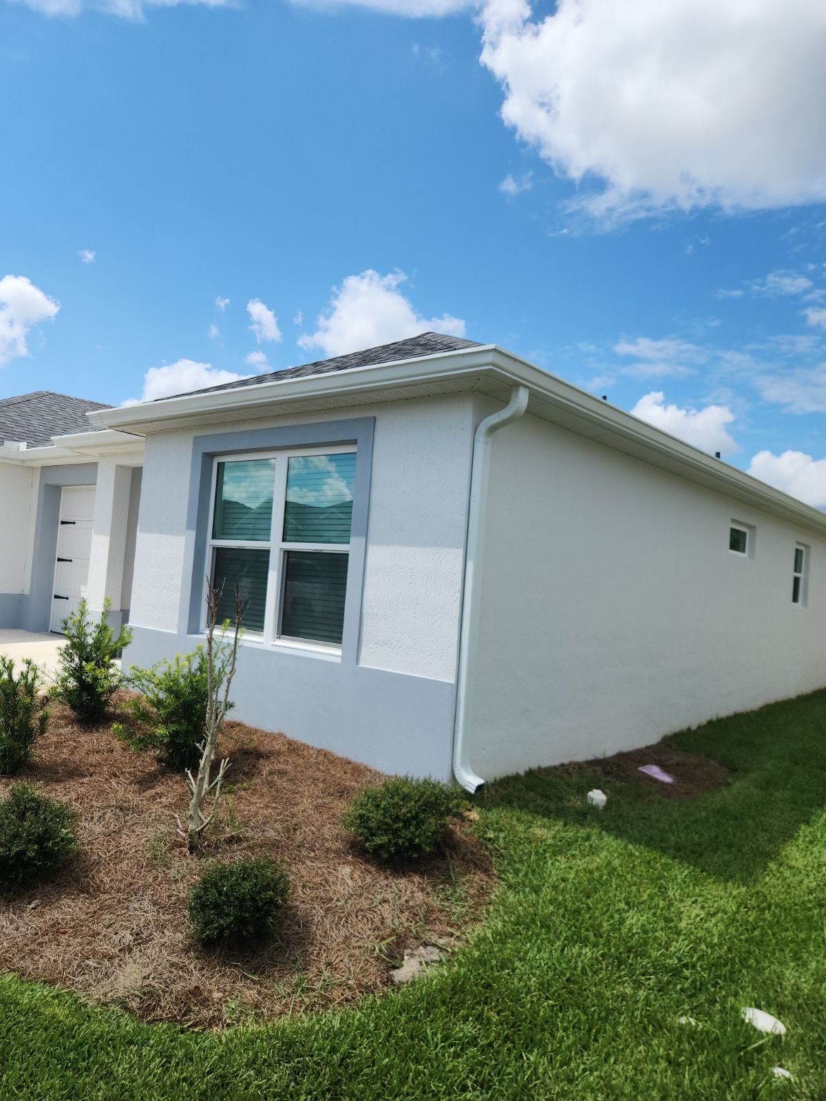 White house exterior with a window, blue trim, and green grass under a blue sky.