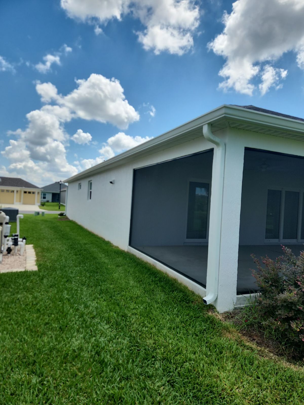 White house with screened porch, green lawn, blue sky with clouds.