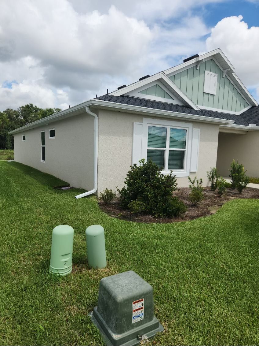 Side view of a light beige house with white trim, green grass, and blue sky with clouds.