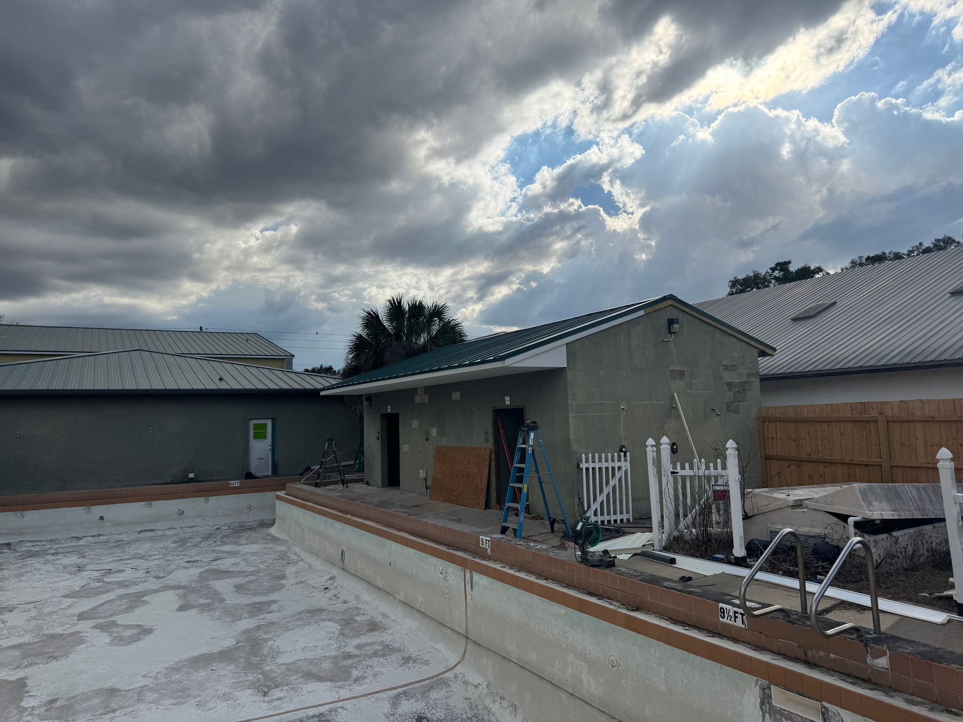 Construction site: empty pool, green stucco building, cloudy sky.