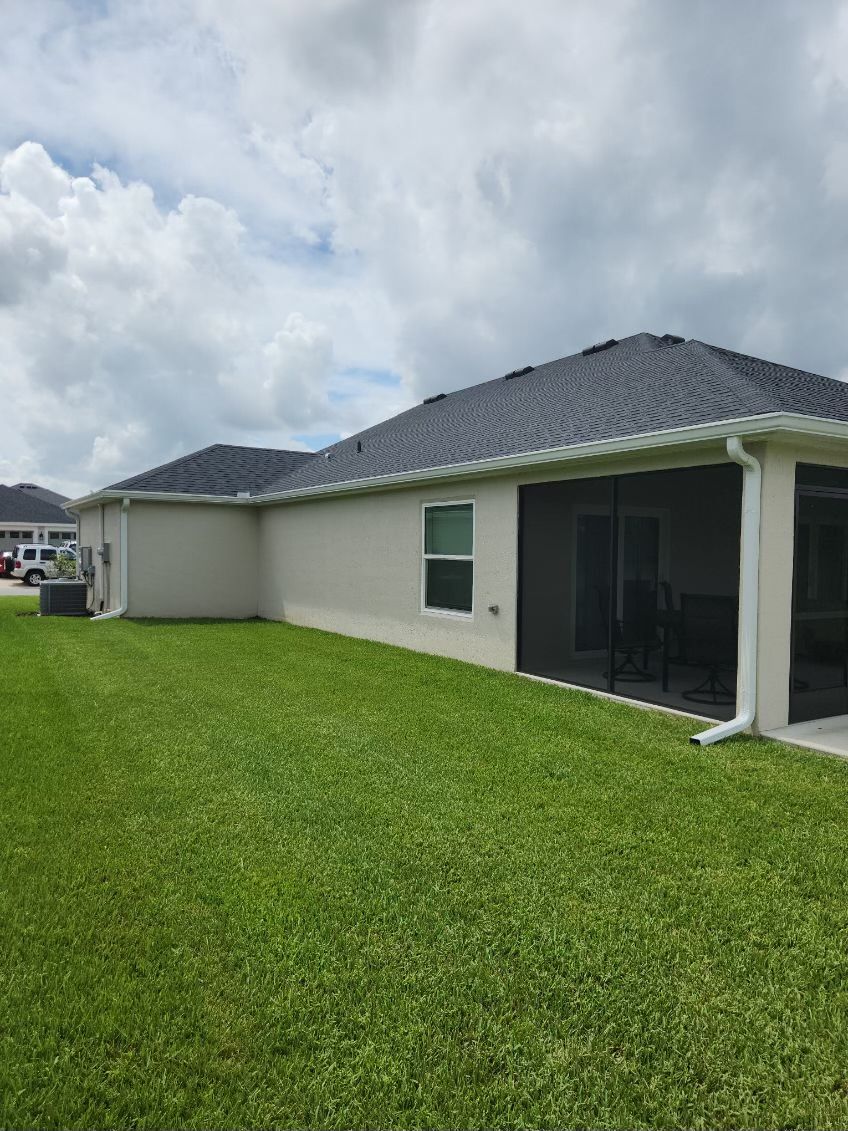 Back view of a house with a gray roof, white trim, a grassy lawn, and a screened patio.