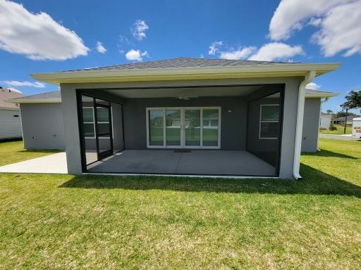 Back view of a grey house with a screened patio, green lawn, and a blue sky with clouds.