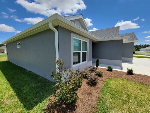 Gray house with white trim, gutter, and window frames; blue sky. Landscaping in foreground.