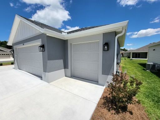 Two-car garage with gray exterior, white doors, black lights, and a concrete driveway on a sunny day.