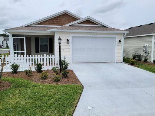 A beige ranch-style house with a white picket fence, a garage, and a driveway.