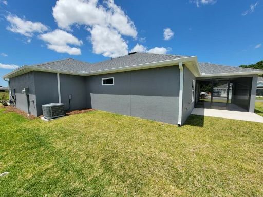 Gray stucco house with white trim, green lawn, and a screened porch under a blue sky with clouds.