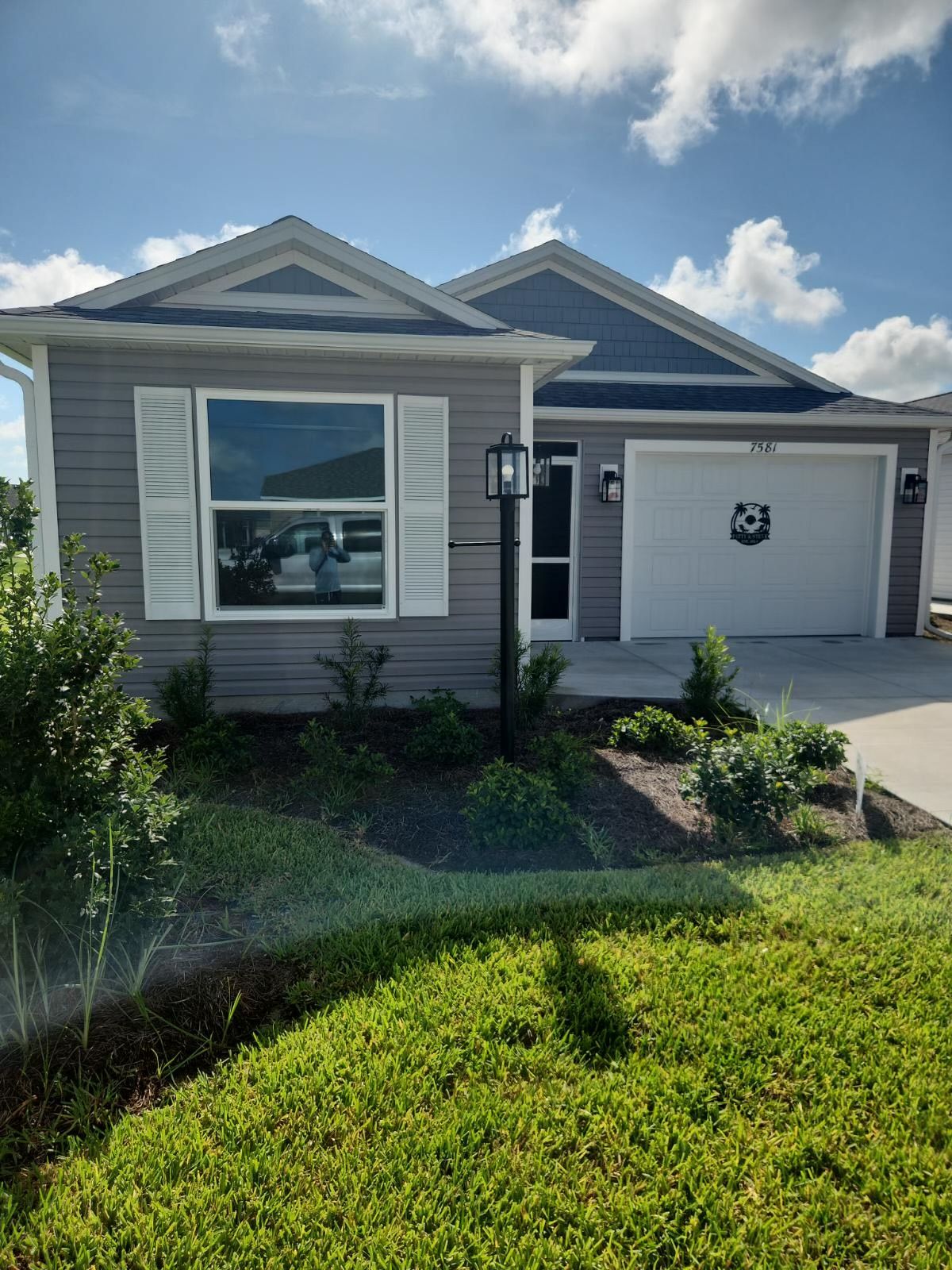Gray house with white trim, blue roof, and green lawn under a partly cloudy sky.