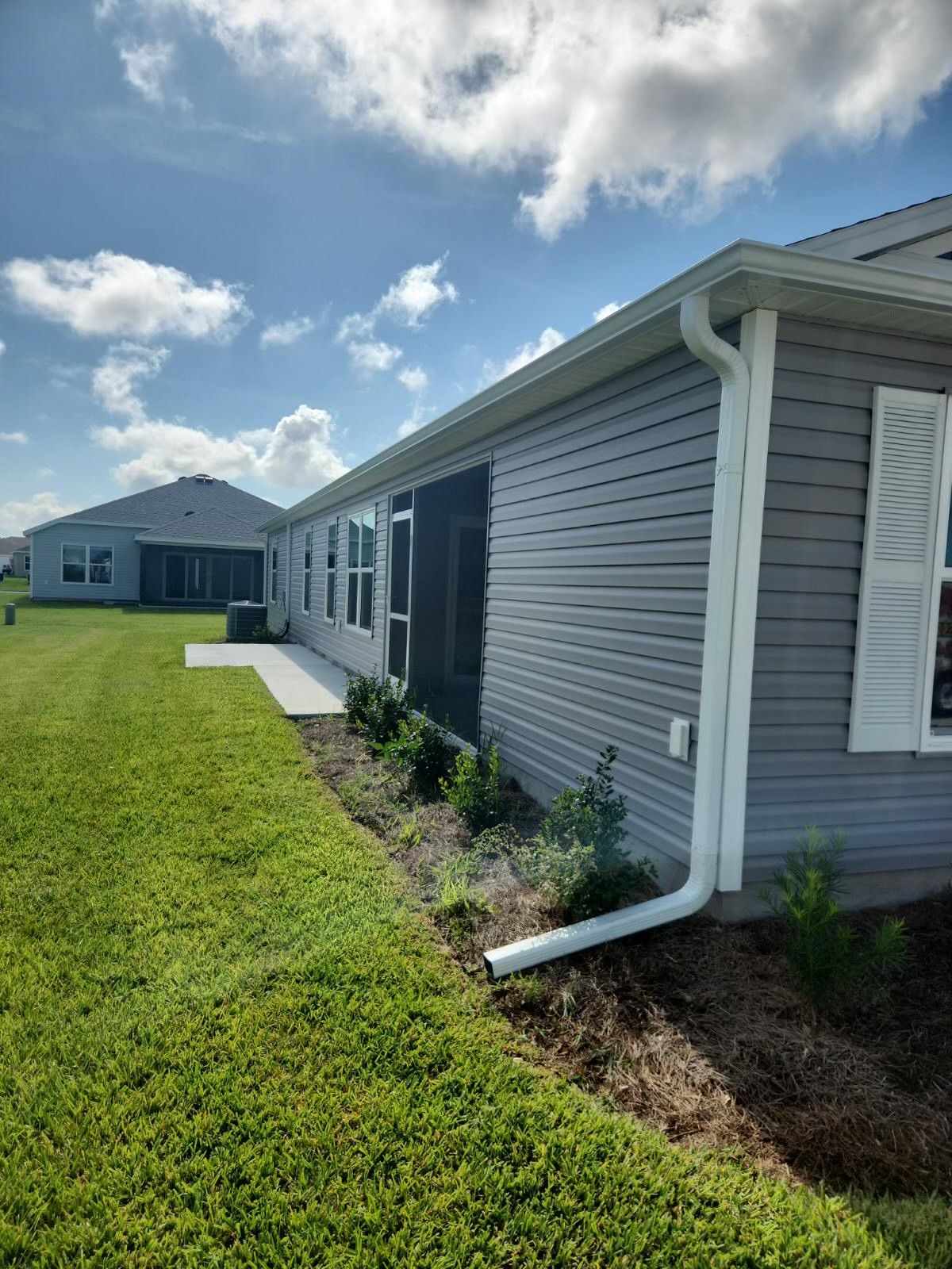 A gray house with white trim and gutter, a green lawn, and a blue sky.
