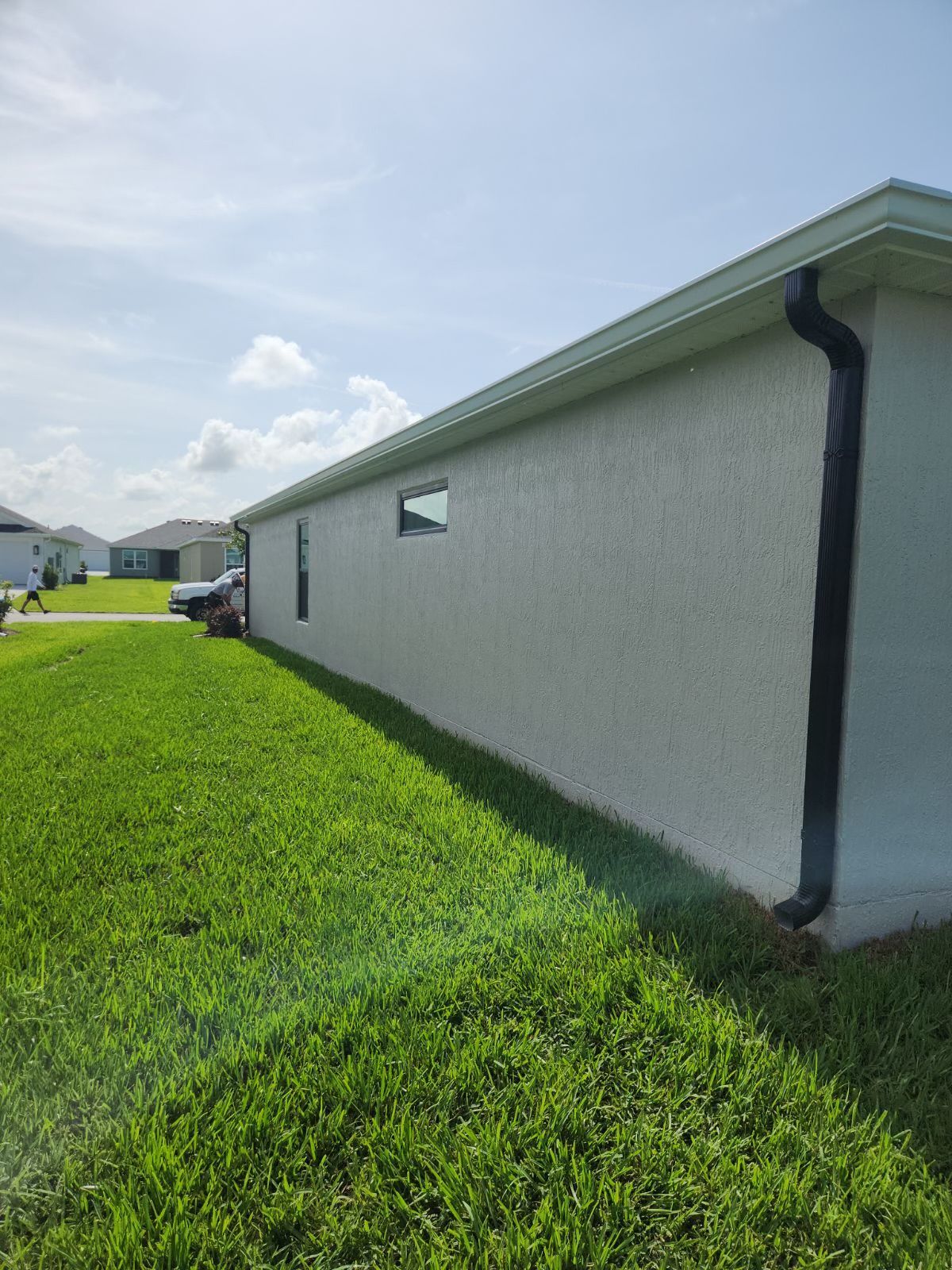 Side view of a house with stucco walls, green lawn, black downspout, and blue sky.