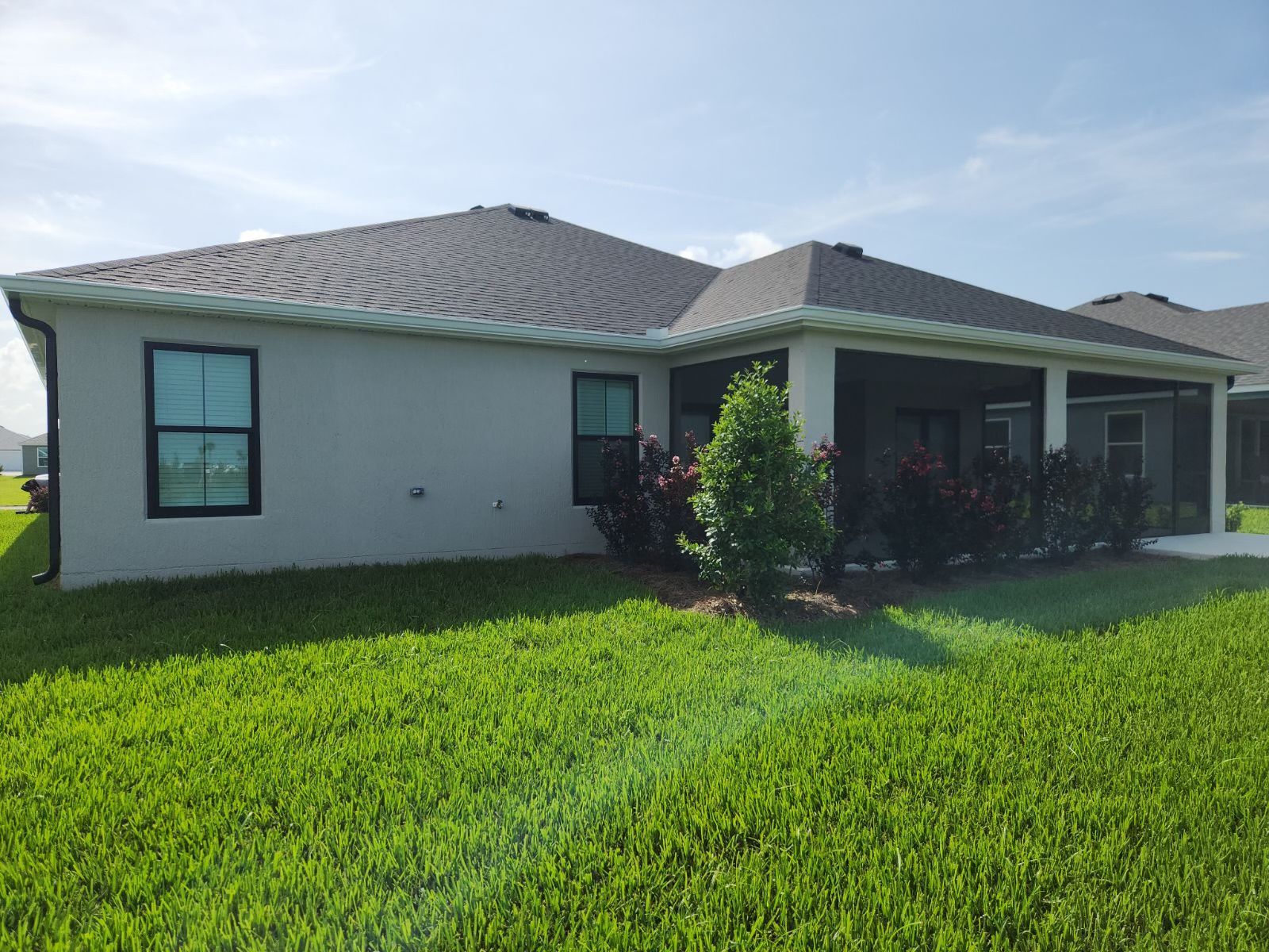 Side view of a light gray house with dark roof, windows, and lush green lawn under a blue sky.
