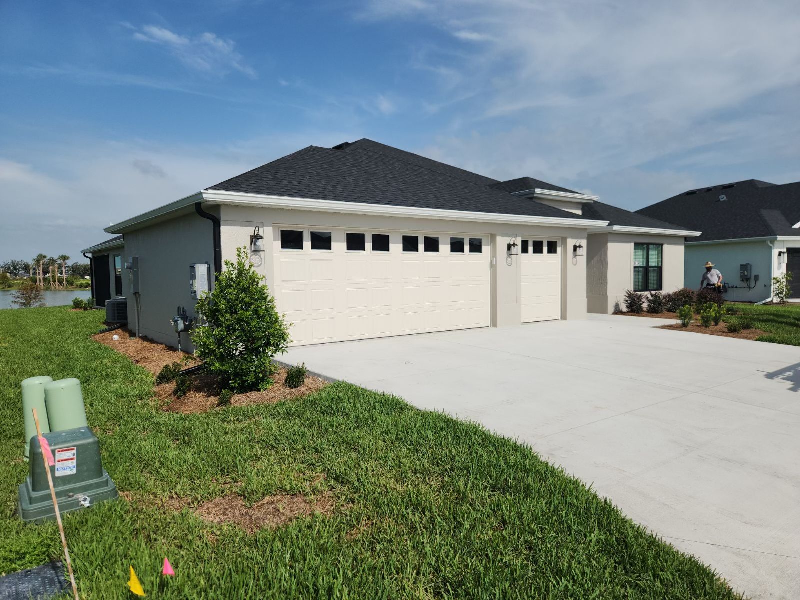 Light gray house with white garage doors, black roof, and concrete driveway.