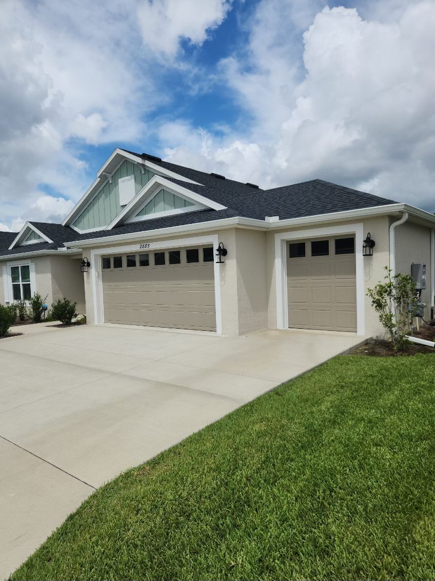 Beige stucco house with tan garage doors, green grass and blue sky with clouds.