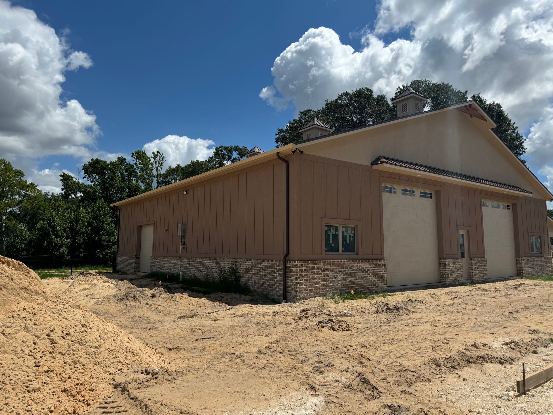 Brown building with stone base and two garage doors, under a blue sky with clouds.