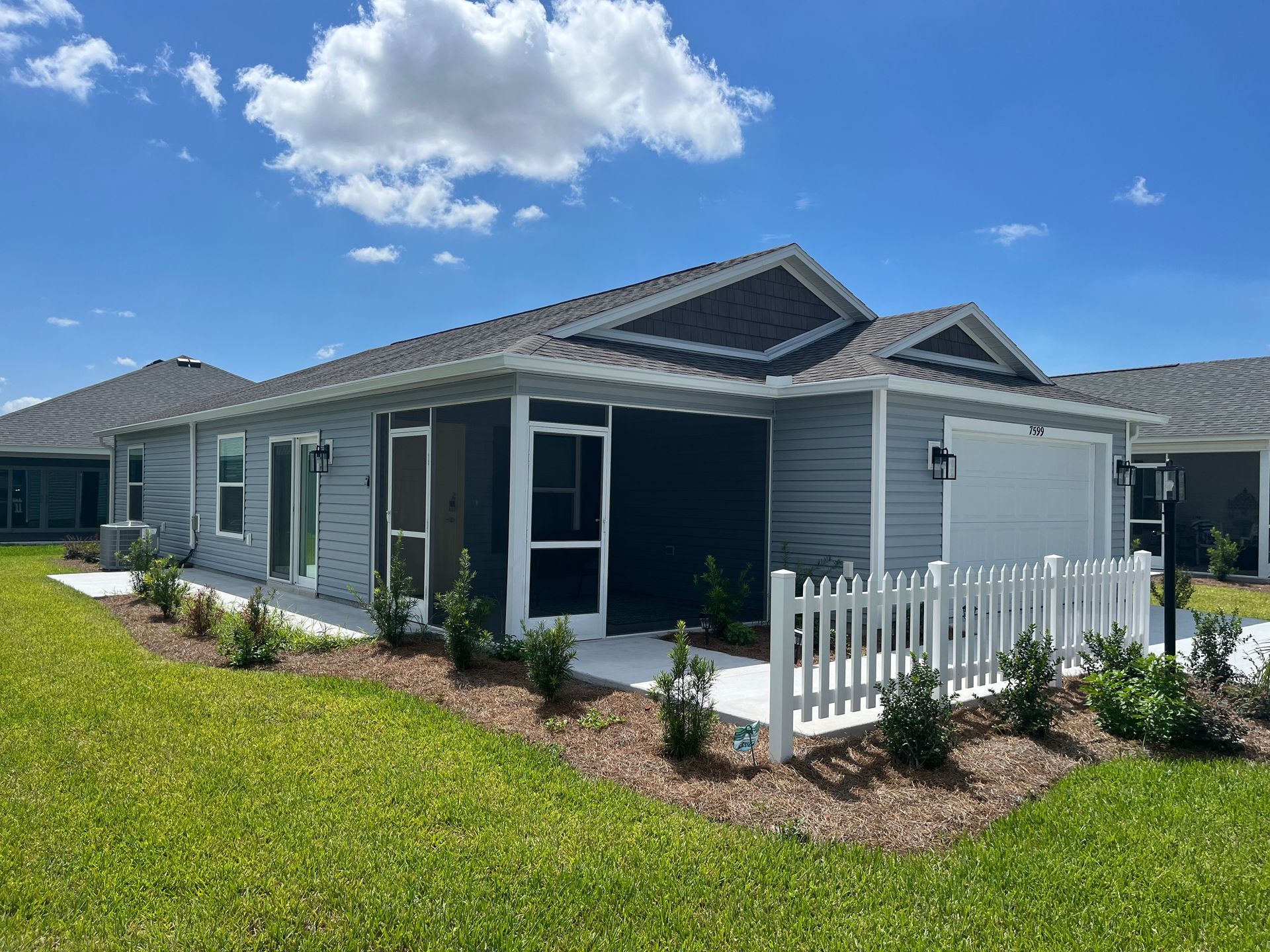A light blue house with a white picket fence, green grass, and a blue sky with clouds.