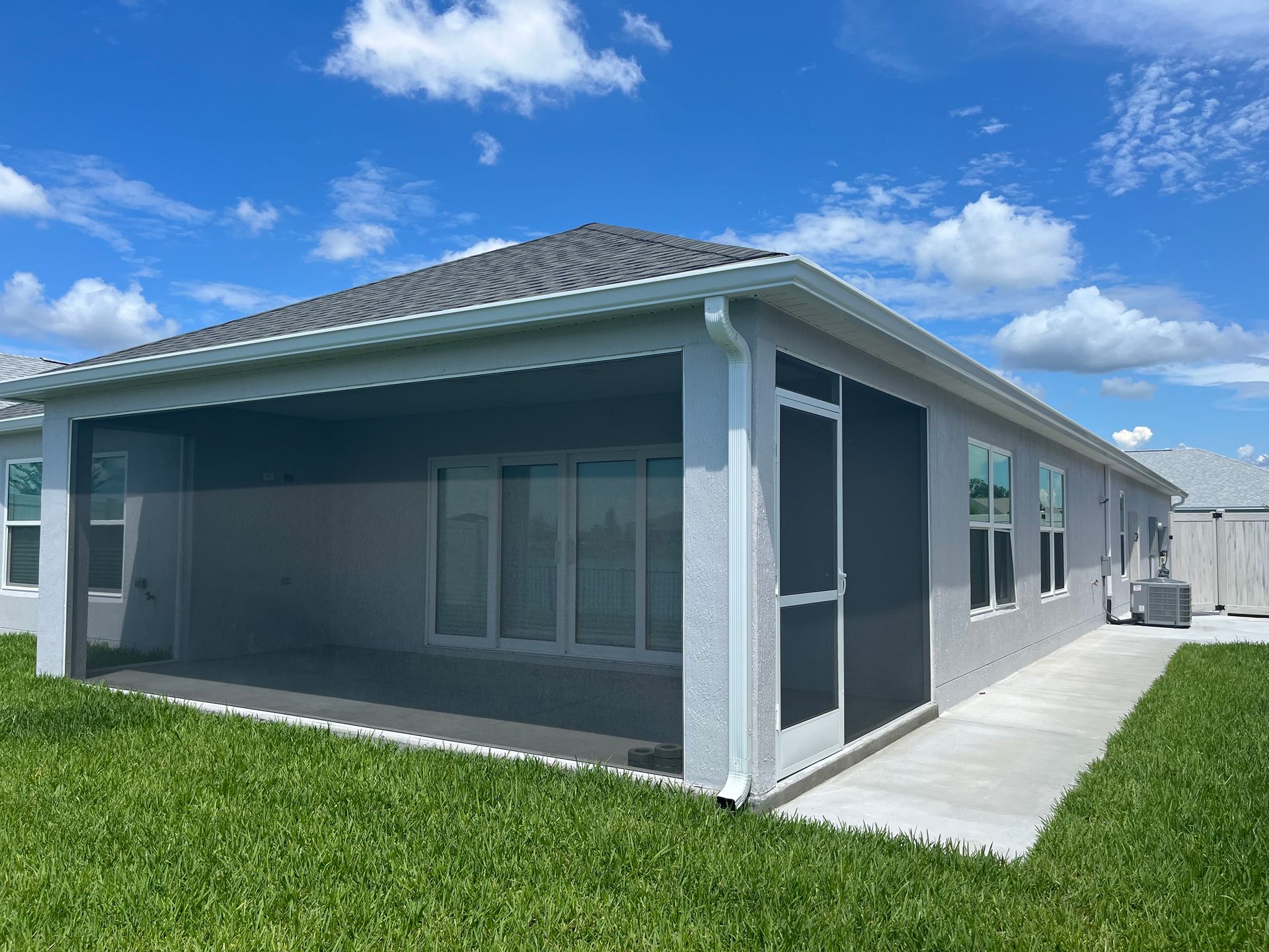 Gray house with screened patio, concrete path, green grass, and blue sky.