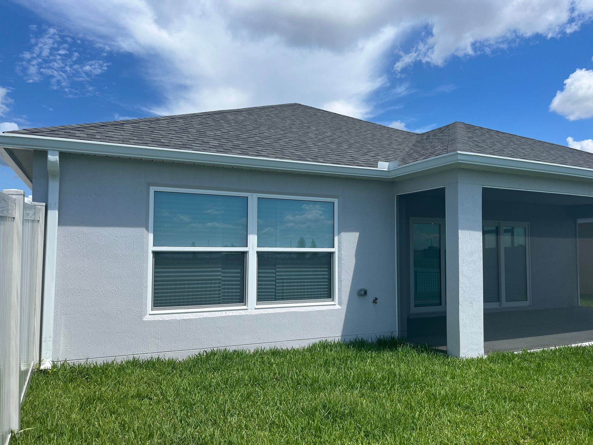 Gray stucco house with a dark gray tiled roof and windows, sunny outdoor setting.