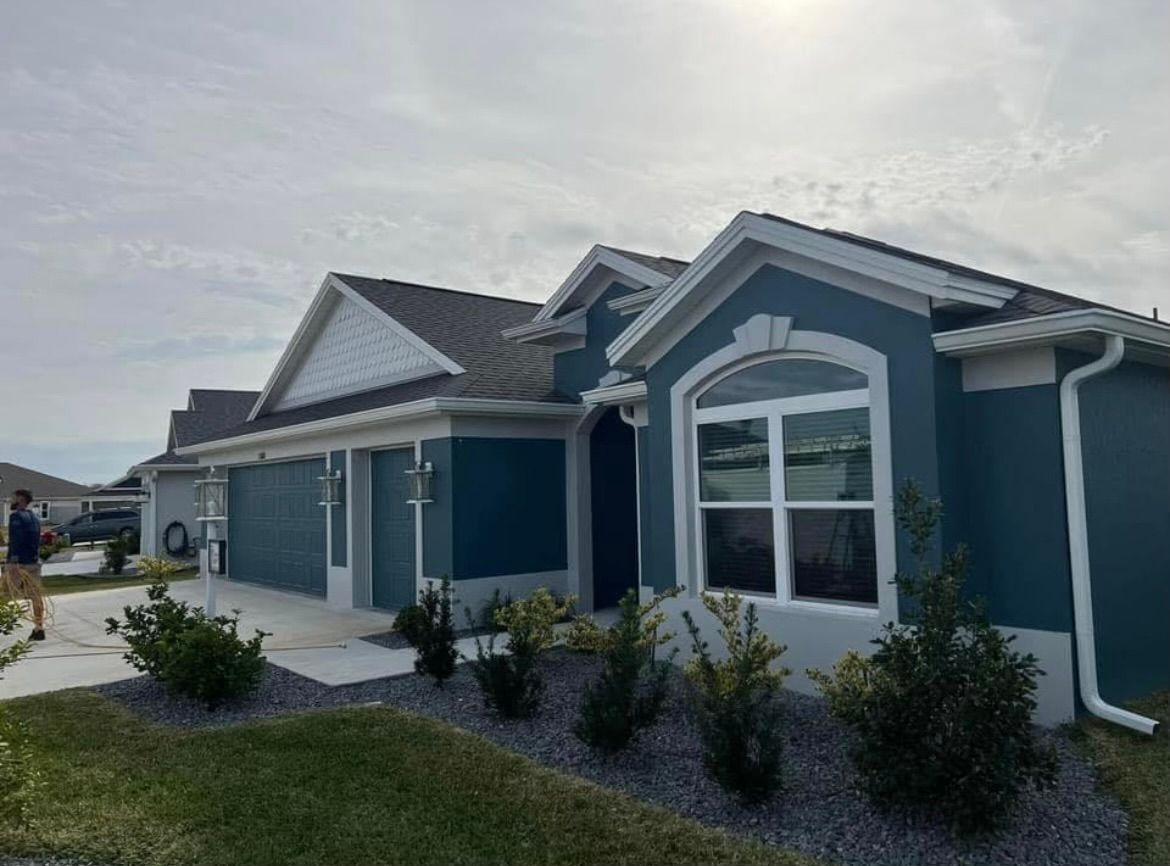Blue house with white trim, gray roof, and landscaping. Cloudy sky.