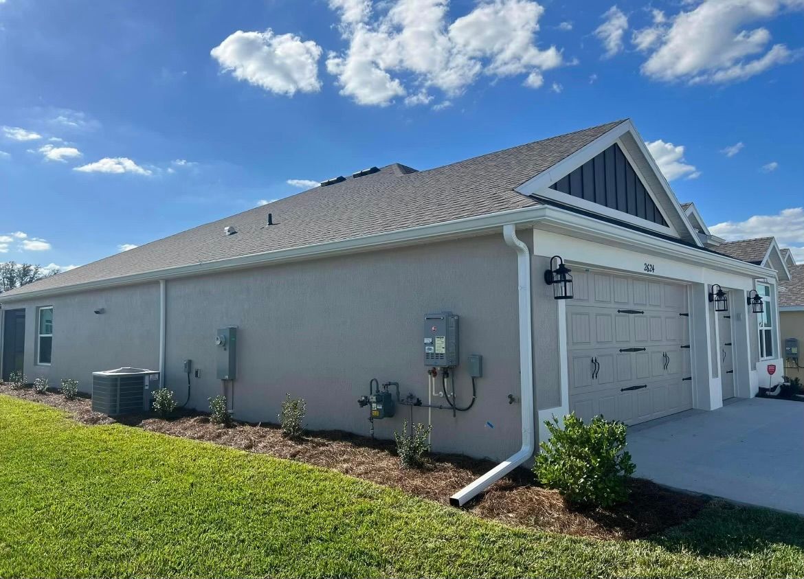 Side view of a light gray house with white trim, green lawn, and a blue sky.