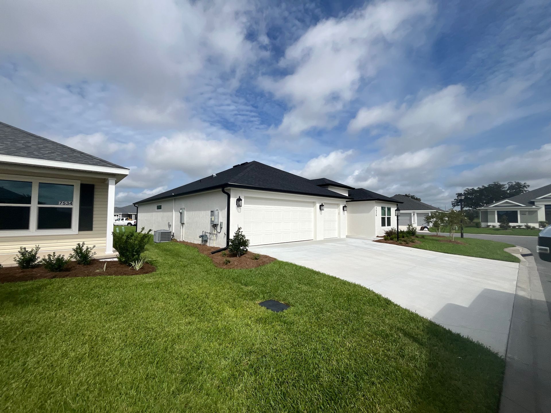 White house with black roof, garage, and green lawn under a cloudy sky.