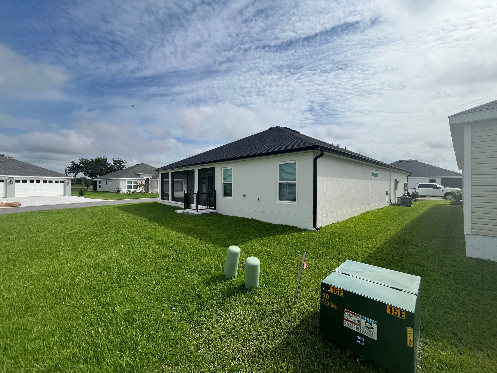 A single-story house with white walls and black roof on a green lawn under a partly cloudy sky.