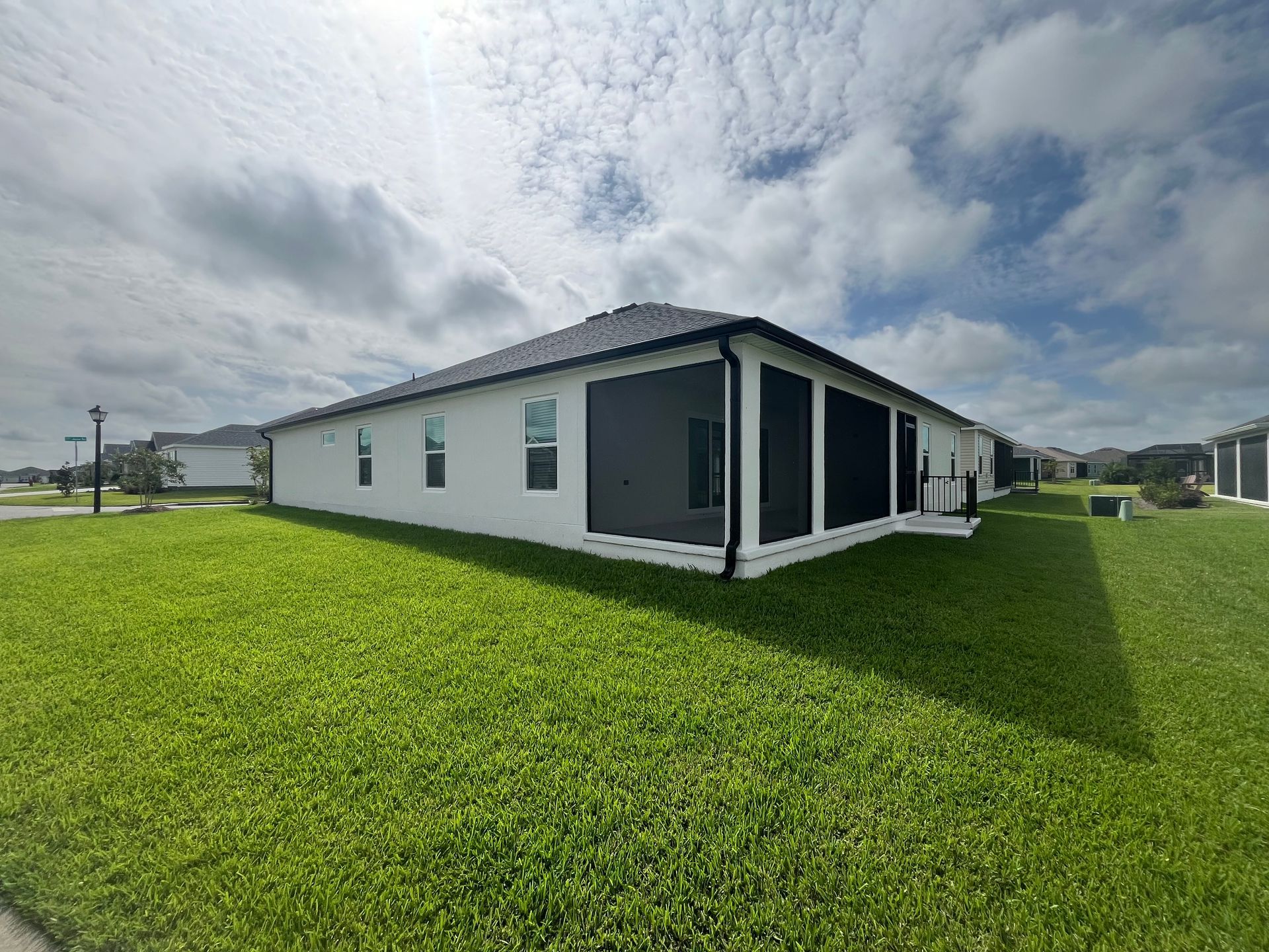 White house with a black-screened porch, green grass, and a cloudy sky.