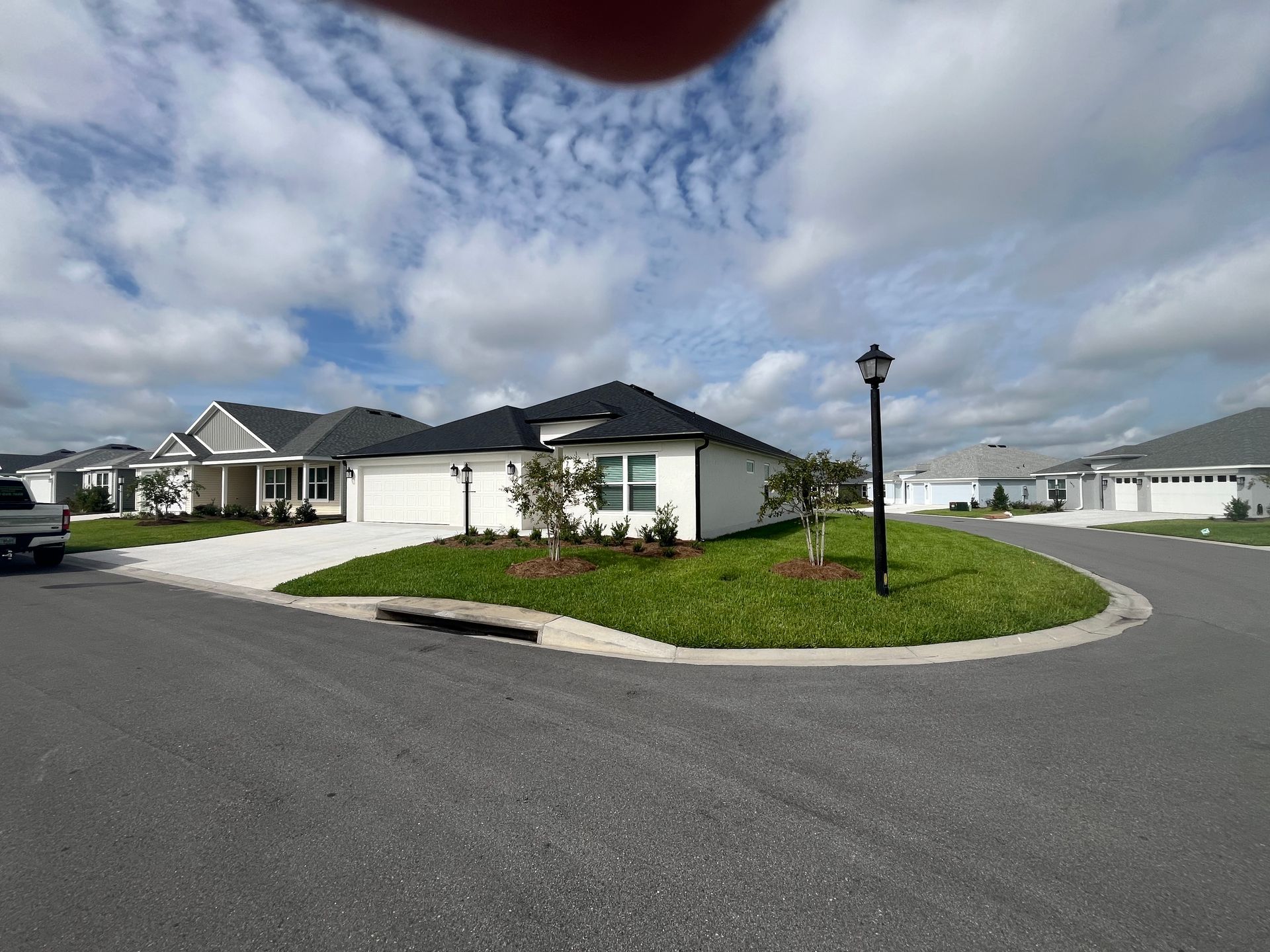 Houses on a street corner, with landscaped beds, blue sky, and a cloudy backdrop.