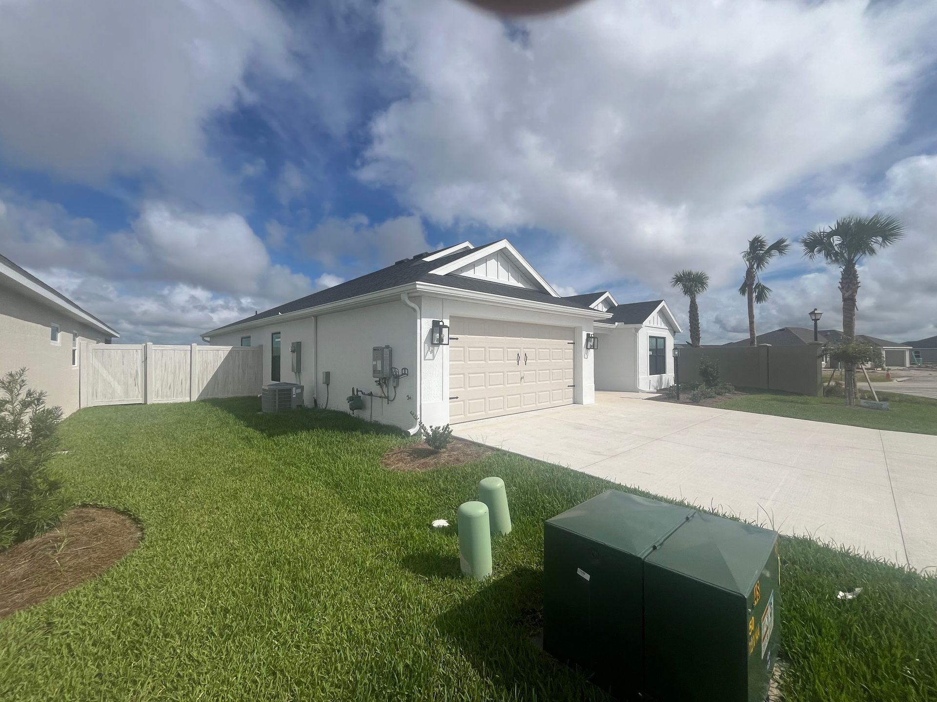 White house with a two-car garage, green lawn, and blue sky with clouds.