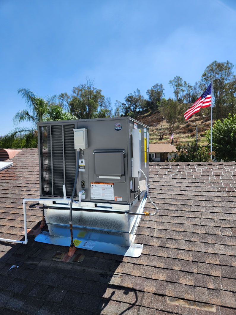 A large air conditioner is sitting on top of a roof next to an american flag.