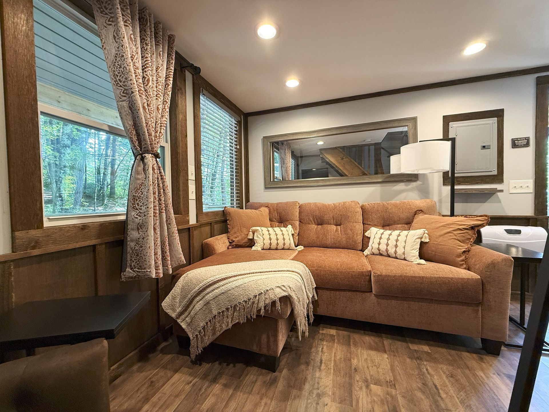 Cozy living room with a brown sectional sofa, large mirror, and window overlooking a green landscape.