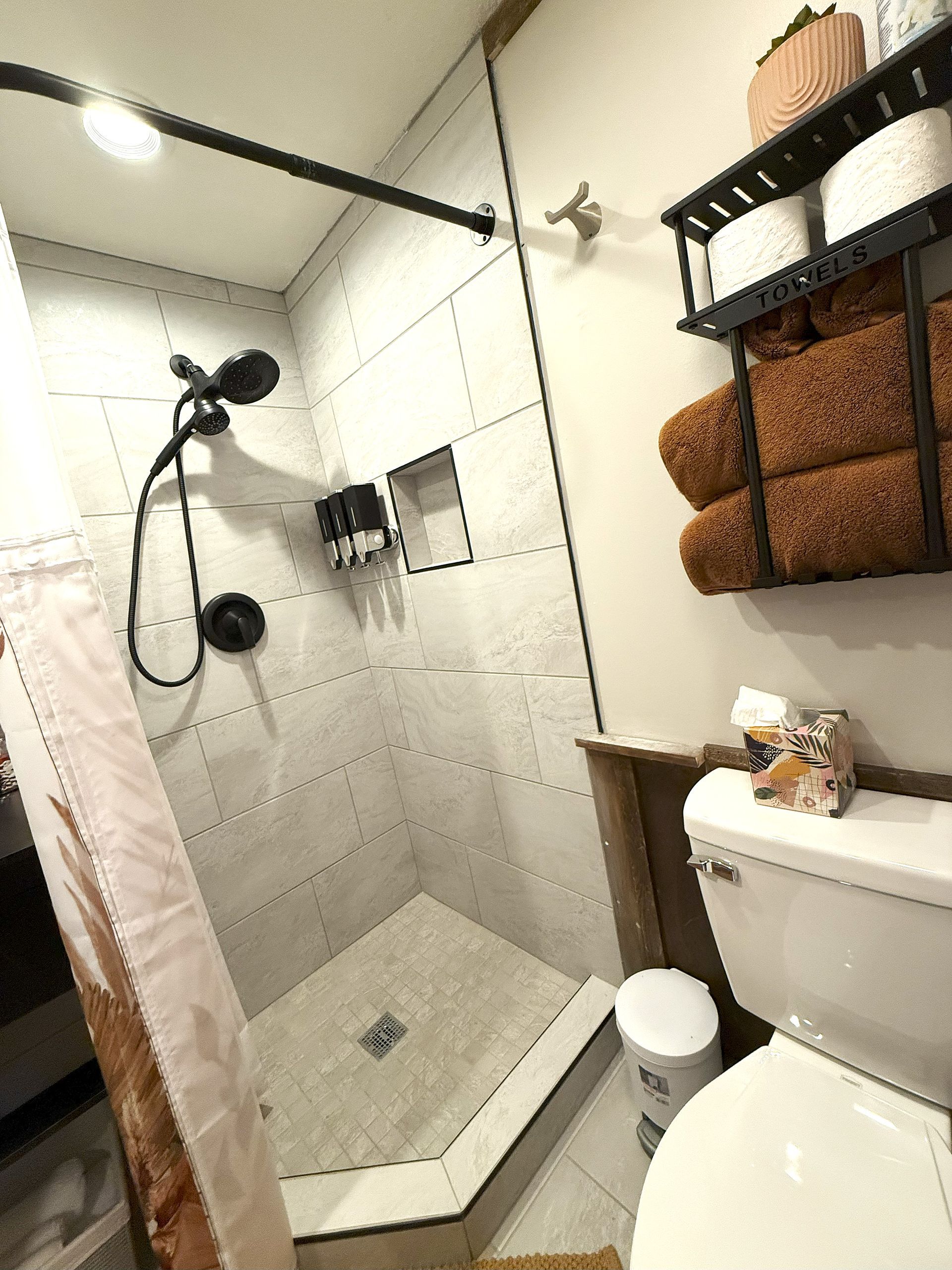 Small bathroom with shower, toilet, towels on a rack, and a basket.