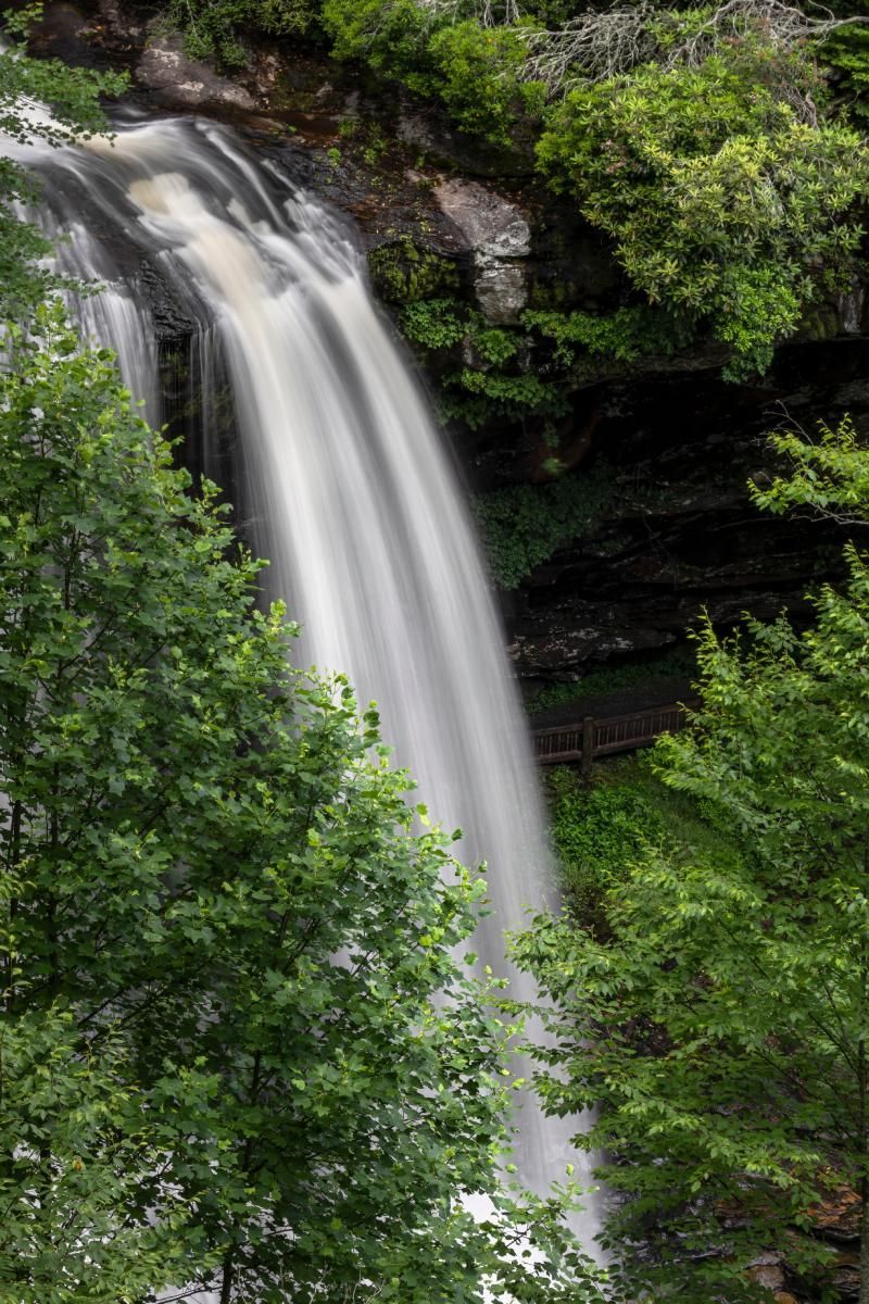 Waterfall cascading down rock face, surrounded by lush green trees.