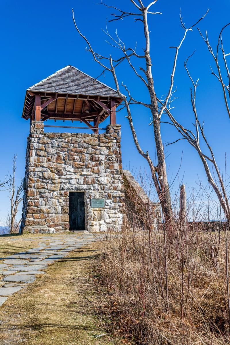 Stone tower with a wooden roof under a bright blue sky. A path leads to the dark door.