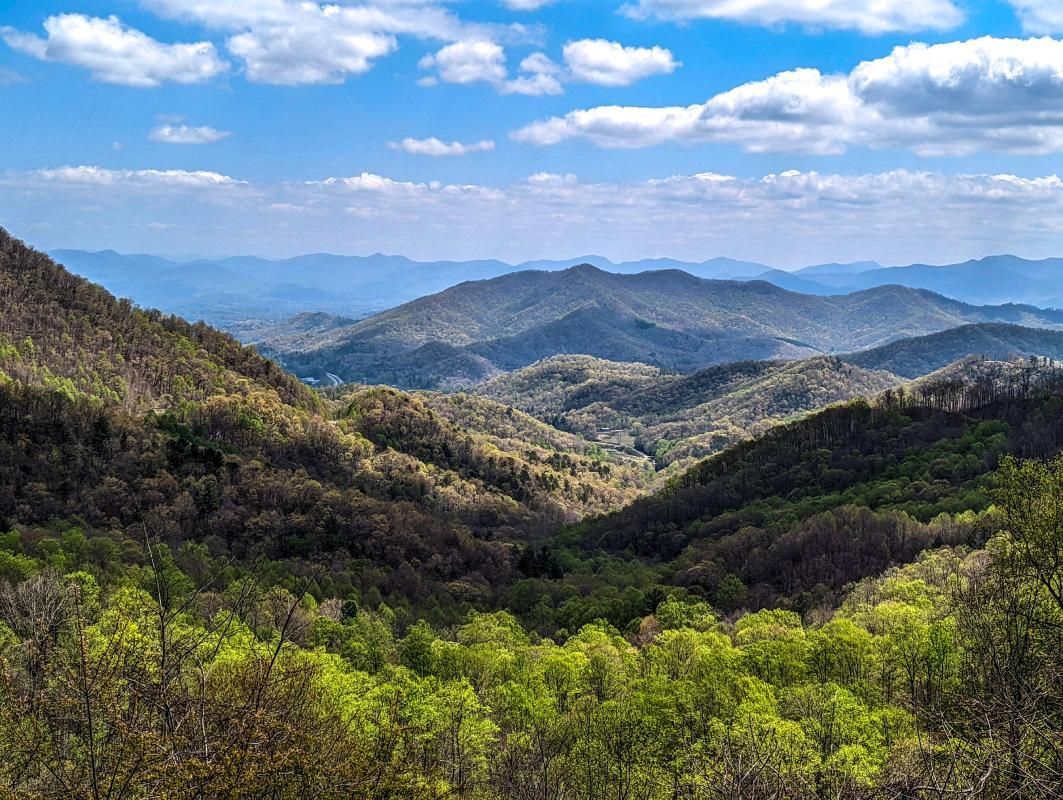Rolling green mountain landscape under a blue sky with fluffy clouds.