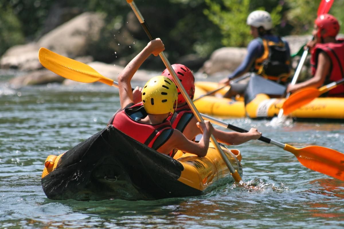 People whitewater rafting in a yellow raft, paddles raised, in a river.