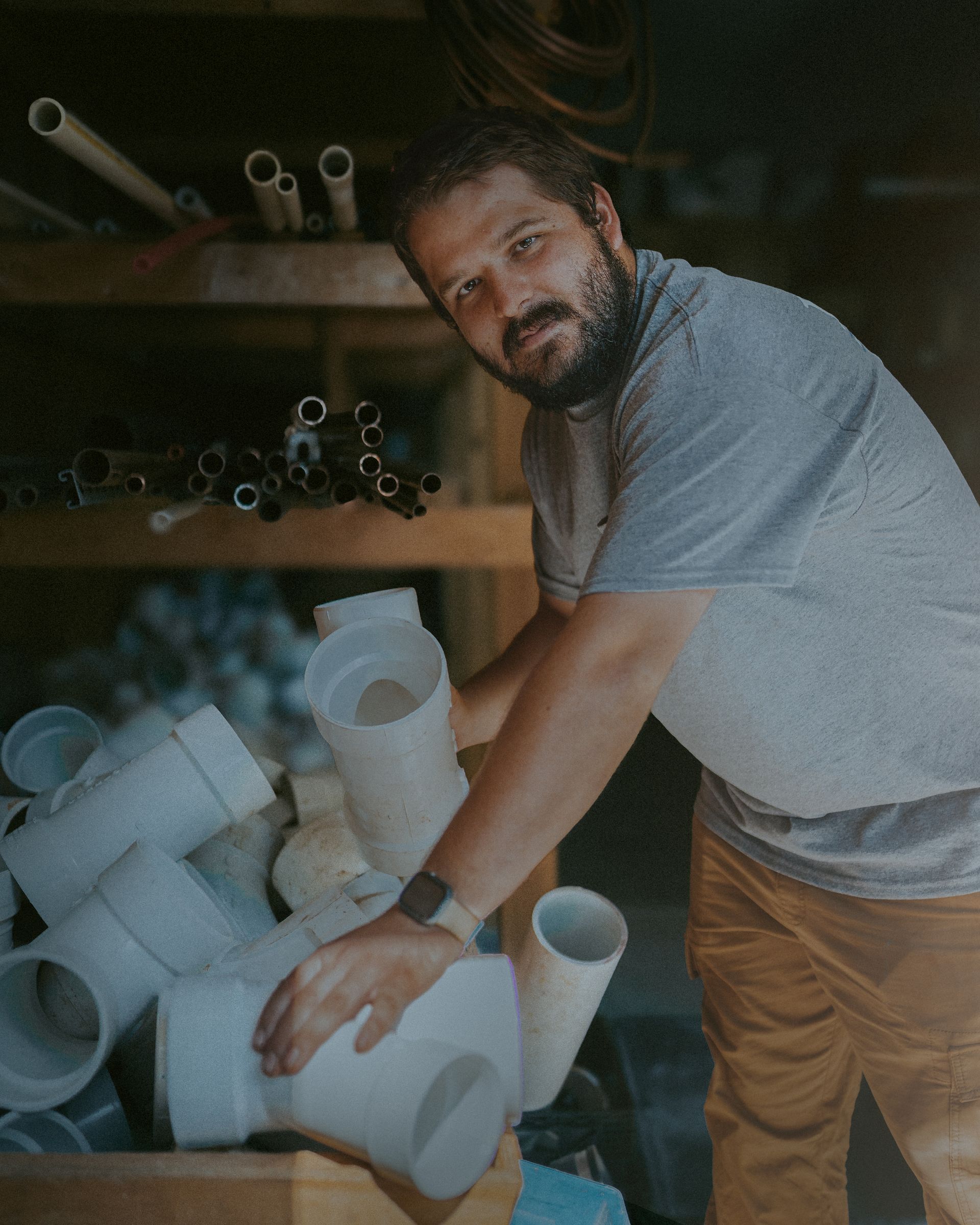 Man holding white PVC pipes in a storage area; dark shelves with pipes in the background.