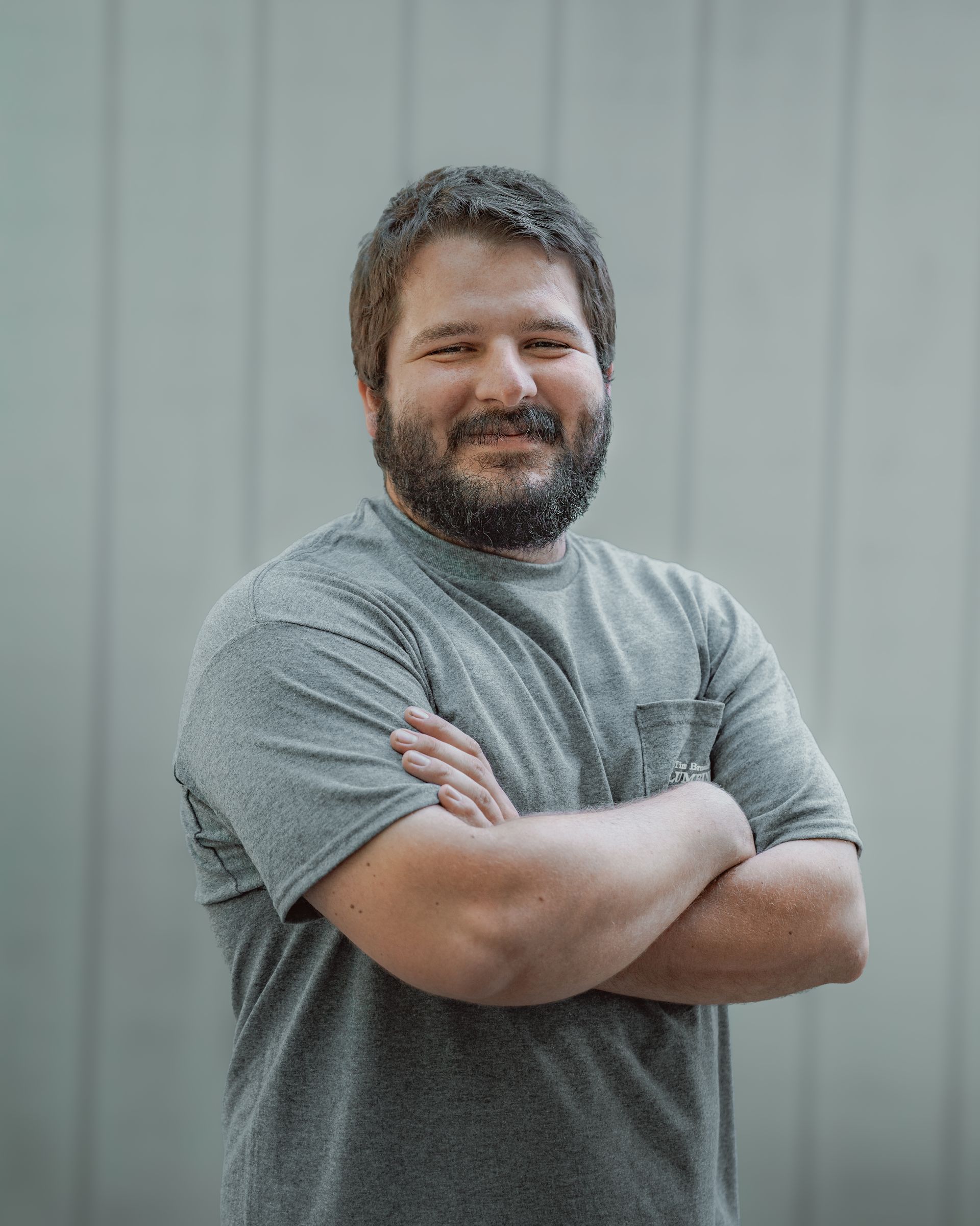 Man with beard and crossed arms smiling in front of a light gray wall.