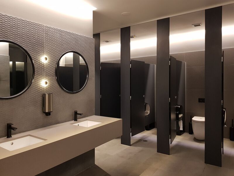 Modern public restroom with sinks, mirrors, and stalls. Gray and black color scheme.