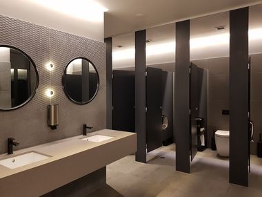 Modern public restroom with sinks, mirrors, and stalls. Gray and black color scheme.