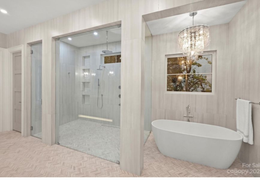 Modern bathroom with a glass shower, soaking tub, and crystal chandelier.