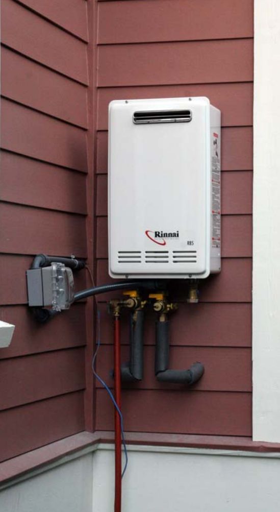 A white, wall-mounted Rinnai tankless water heater on a maroon-sided building.