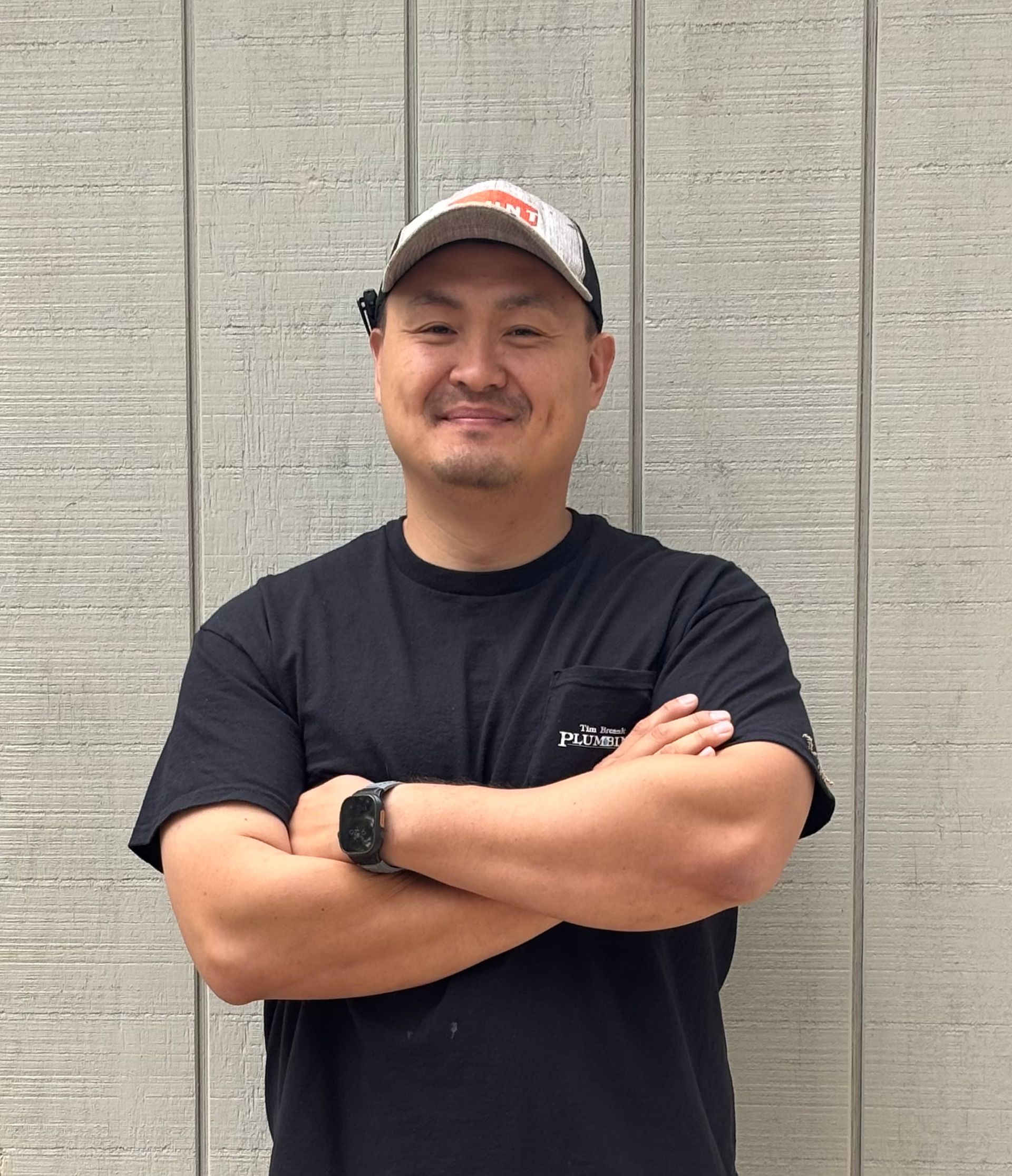 Man with beard and crossed arms smiling in front of a light gray wall.