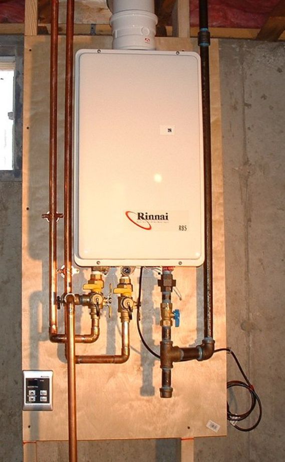 Tankless water heater mounted on plywood, with copper pipes and black vent.