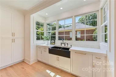 White kitchen with cabinetry, black sink, and large windows overlooking a residential neighborhood.