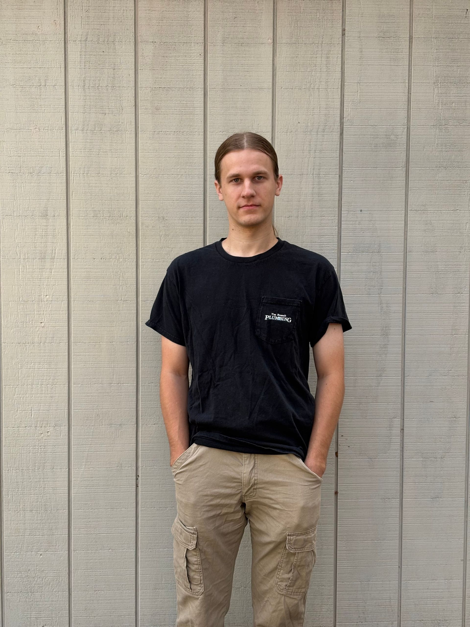 Bald man with crossed arms, wearing a grey t-shirt, smiling, standing outside in front of grey panels.