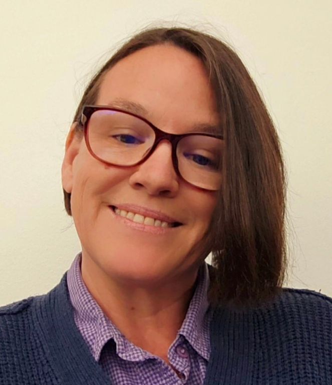 A woman wearing glasses and a blue sweater is smiling for the camera.