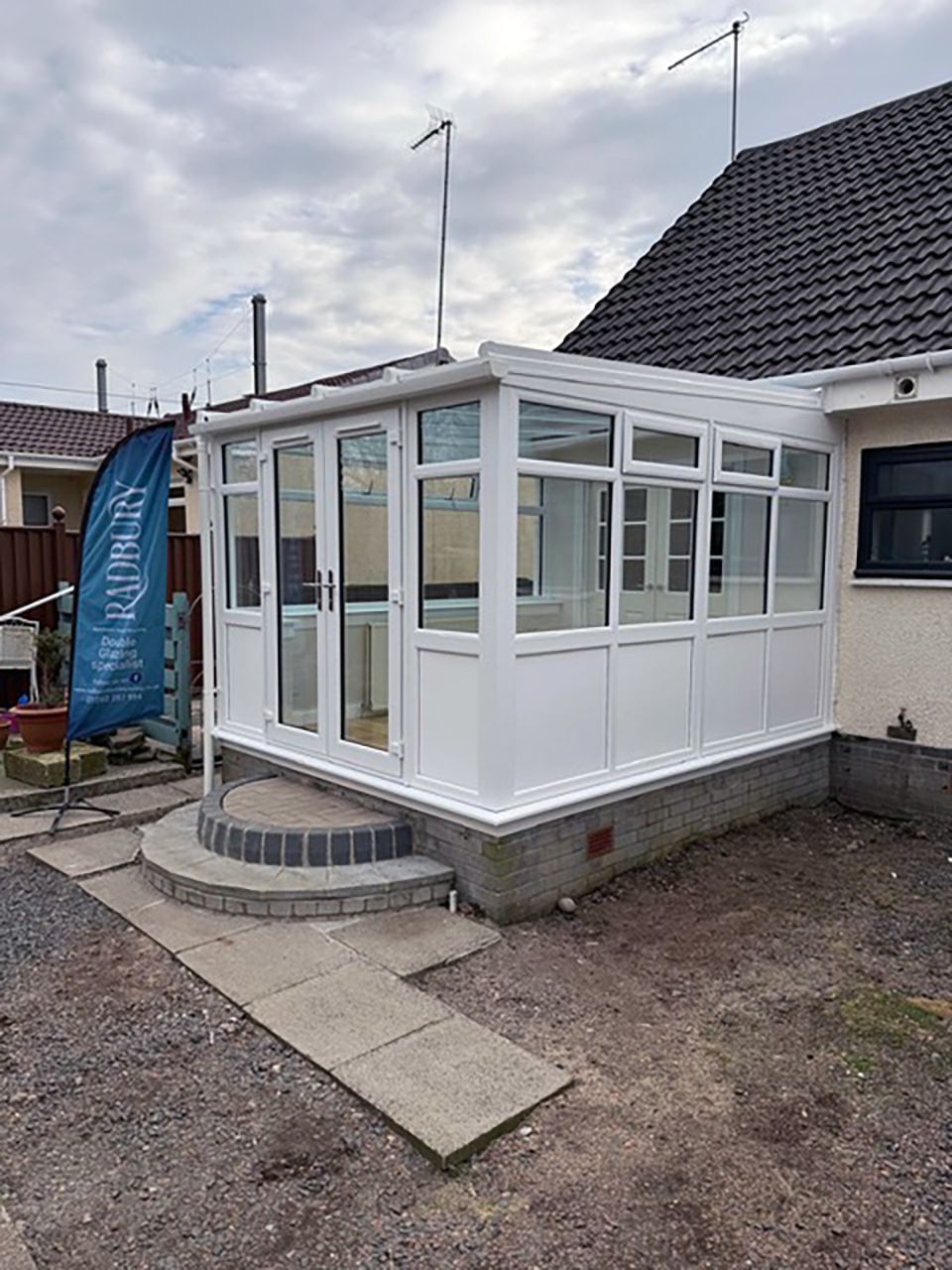 White conservatory with steps and a ramp next to a house under a cloudy sky.