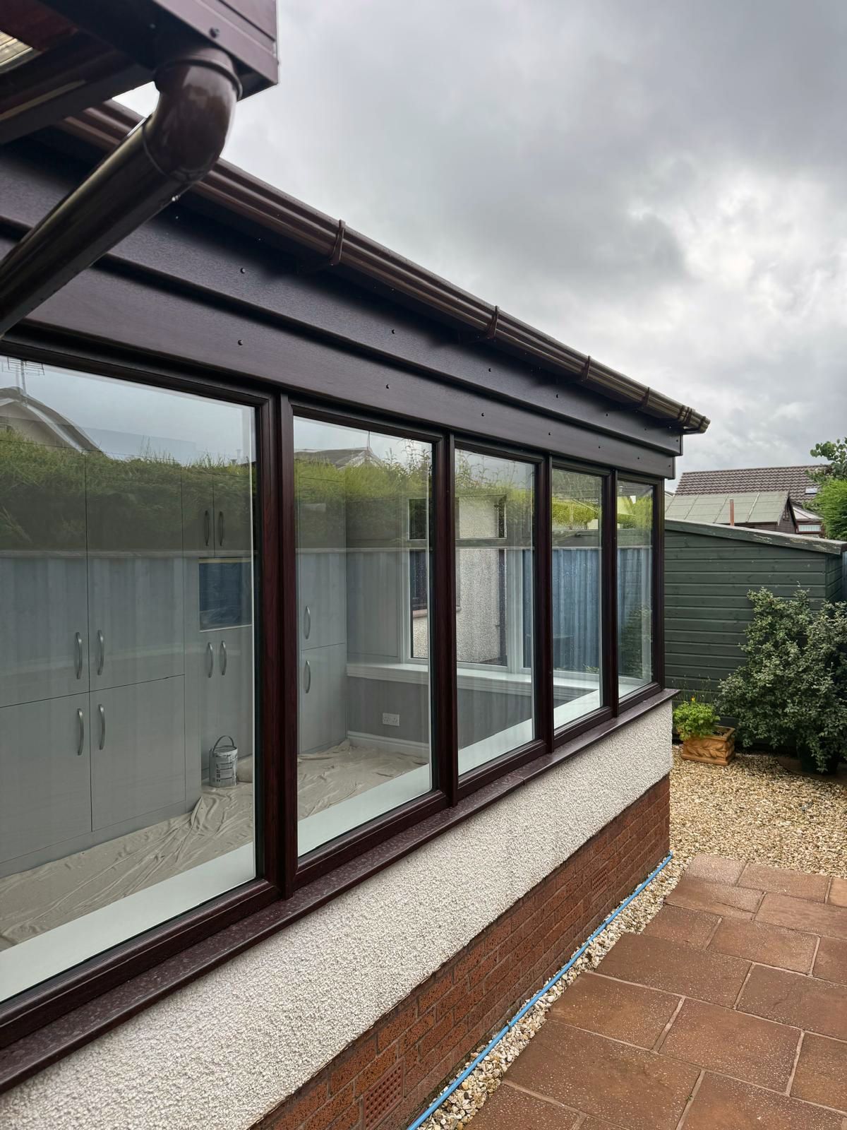 Brown framed windows on a home exterior with a brown roof and gutter under an overcast sky.